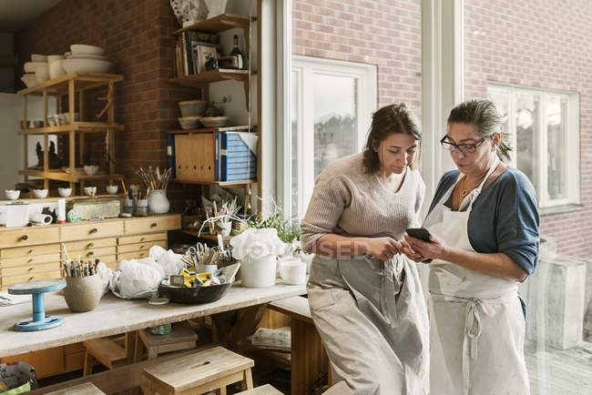 Женщины используют смартфон в мастерской по гончарному делу — стоковое фото
