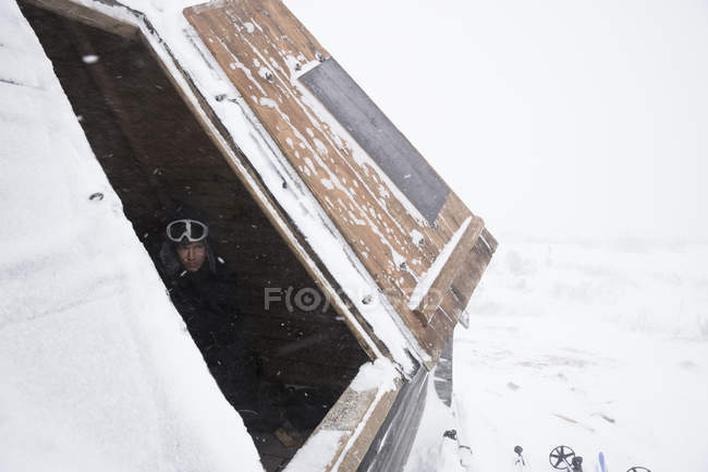 Hombre en el techo de la cabaña de madera con nieve - foto de stock