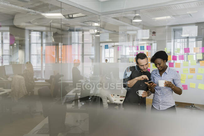 Coworkers with smartphone and coffee cups in office — Stock Photo