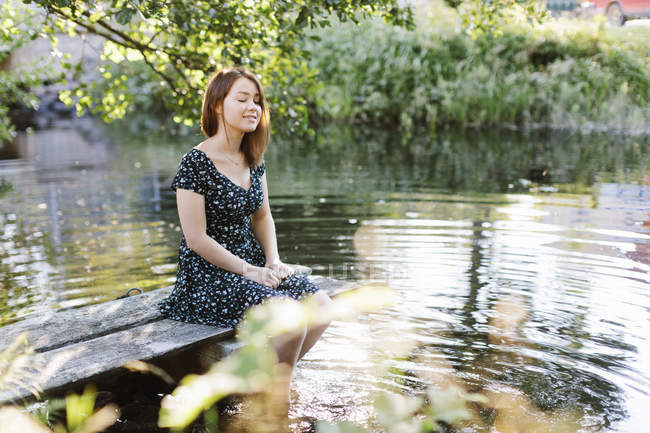 Junge Frau sitzt am See und konzentriert sich auf den Vordergrund — Stockfoto