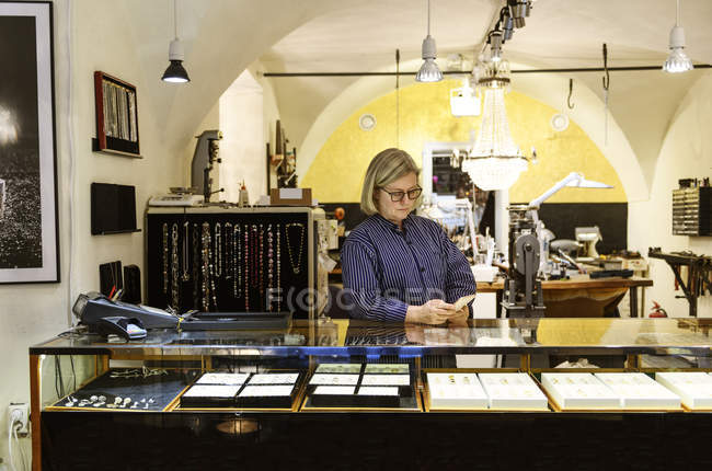 Goldsmith using smart phone at counter of jewellery shop — Stock Photo