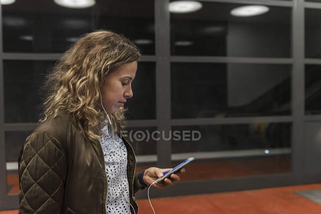 Jeune femme regardant le téléphone cellulaire à la station de métro — Photo de stock