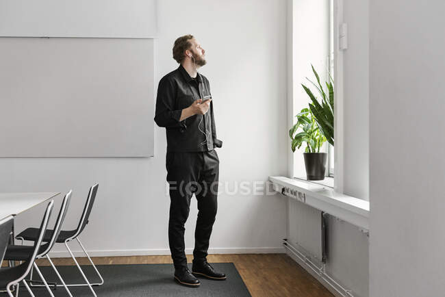 Homem em fones de ouvido usando smartphone na sala de bordo e olhando para a janela — Fotografia de Stock