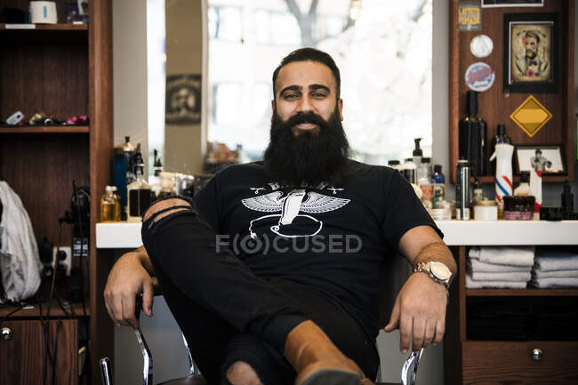 Retrato de barbeiro sentado na cadeira e sorrindo para a câmera — Fotografia de Stock