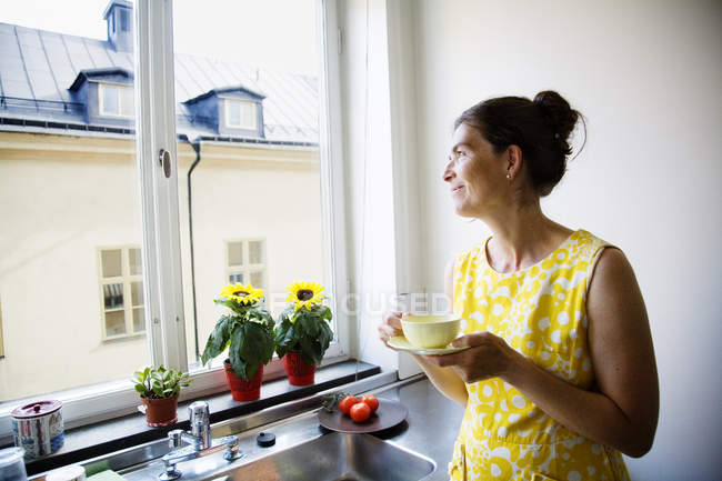 Mulher bebendo café e olhando através da janela — Fotografia de Stock