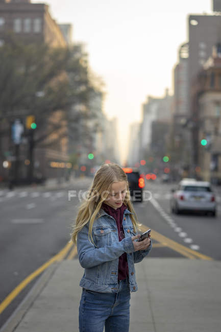 Chica adolescente sosteniendo el teléfono celular en la calle de la ciudad - foto de stock