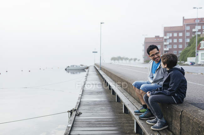 Padre e hijo sentados junto al puerto - foto de stock