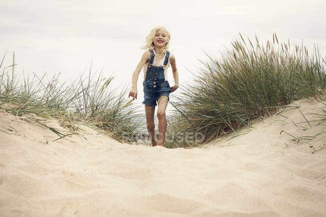 Chica vistiendo overoles de mezclilla caminando en la duna de arena - foto de stock