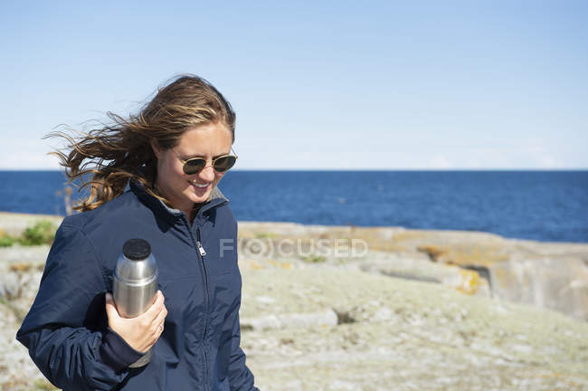 Frau hält Thermoskanne auf Felsen am Meer — Stockfoto