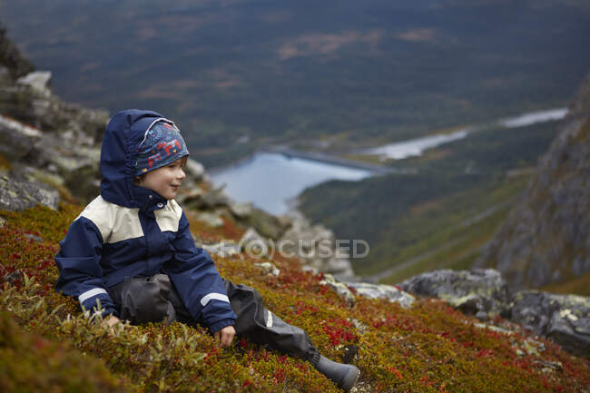 Mignon gai petit garçon assis sur la montagne — Photo de stock