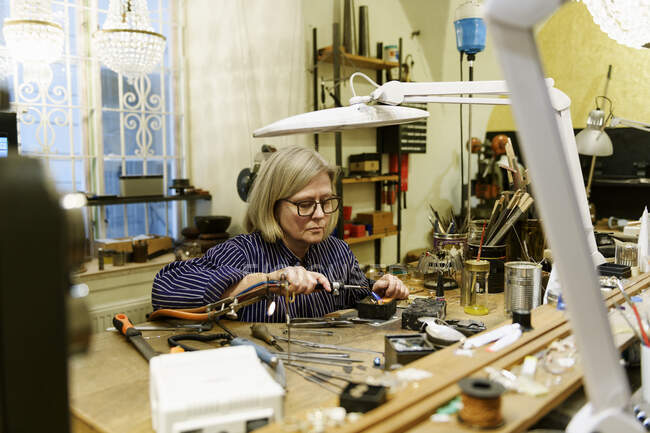 Goldsmith sitting at desk and working in her workshop — Stock Photo