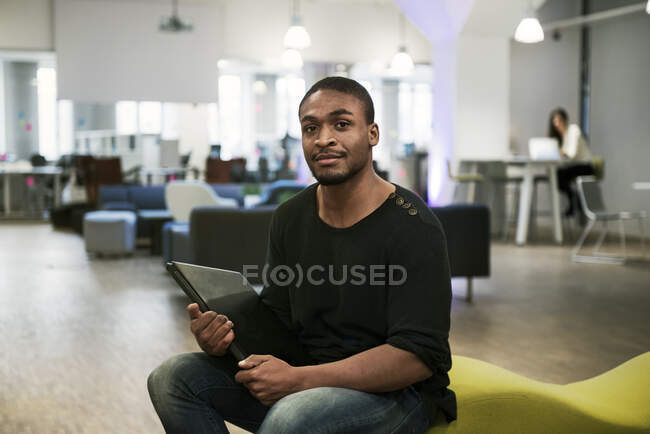 Чоловік середнього віку тримає ноутбук і дивиться на камеру, сидячи на дивані в офісі — стокове фото