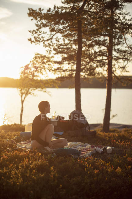 Jovem mulher sentada no cobertor de piquenique pelo Lago Norra Bredsjon, Suécia — Fotografia de Stock