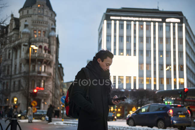 Молодий чоловік використовує мобільний телефон під час прогулянки по міській вулиці — стокове фото