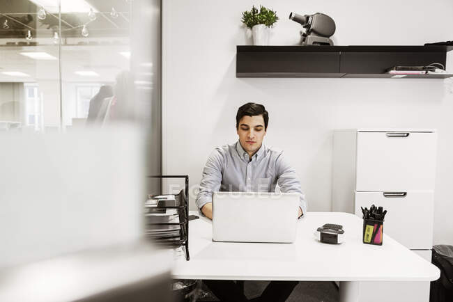 Hombre joven usando el portátil en el escritorio en la oficina - foto de stock
