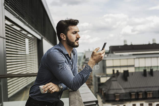 Молодой человек смотрит на сотовый телефон на балконе — стоковое фото