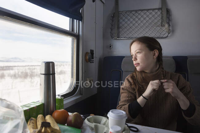 Женщина сидит за столом и смотрит в окно поезда — стоковое фото