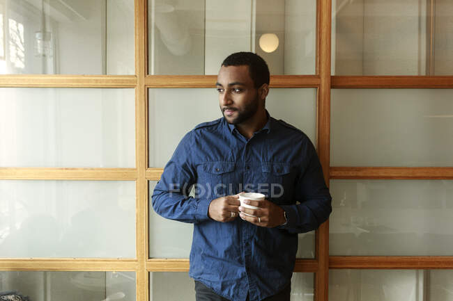 Портрет бизнесмена с чашкой кофе, стоящего в офисе — стоковое фото