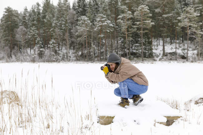 Mulher agachada tirando foto na neve — Fotografia de Stock