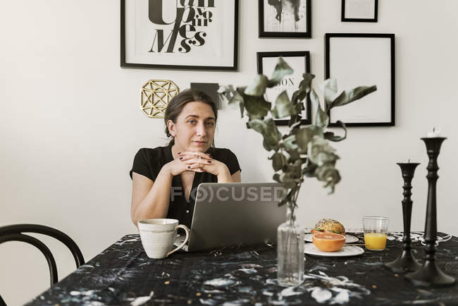 Mujer joven usando el ordenador portátil durante el desayuno - foto de stock