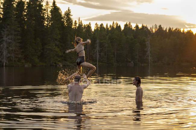 Man throwing teenage girl over lake at sunset — Stock Photo