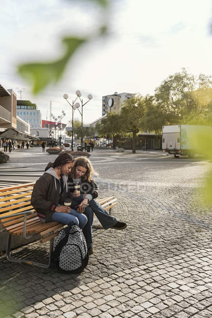 Teenage girls using smart phone on bench — Stock Photo