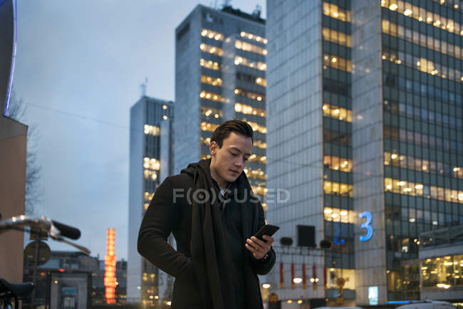 Young man using cell phone while walking down city street — Stock Photo