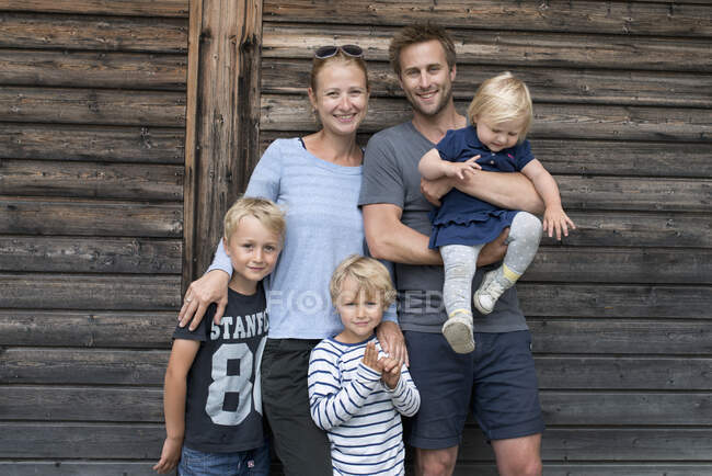 Família posando ao ar livre perto de casa de madeira e sorrindo para câmera — Fotografia de Stock