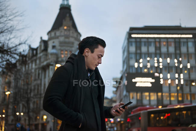 Young man holding cell phone walking down city street — Stock Photo