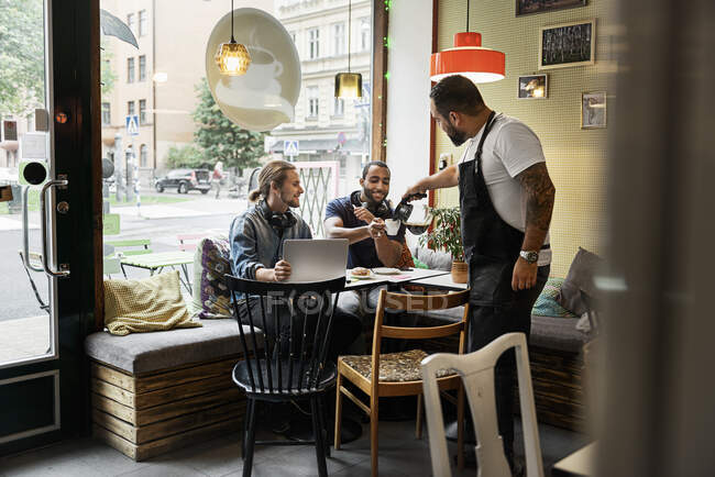 Barista pouring coffee and serving young men in cafe — Stock Photo