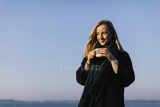 Giovane donna che tiene la tazza contro il cielo limpido — Foto stock