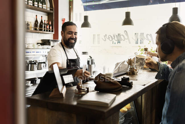 Смолящий бариста обслуживает молодого человека в кафе — стоковое фото