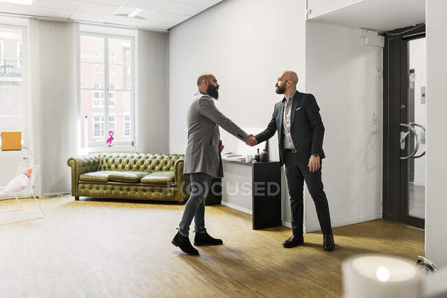 Uomini che scuotono le mani in ufficio, vista completa lunghezza — Foto stock