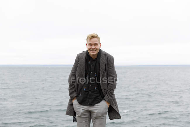 Uomo sorridente che indossa un cappotto grigio presso il lago Vattern nella Riserva Naturale di Stora Lund, Svezia — Foto stock