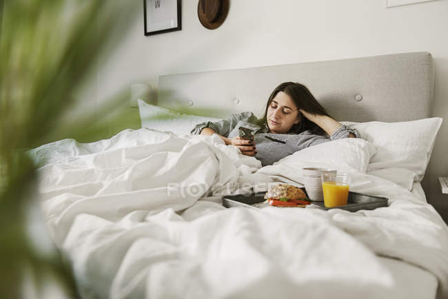 Young woman using smart phone in bed — Stock Photo