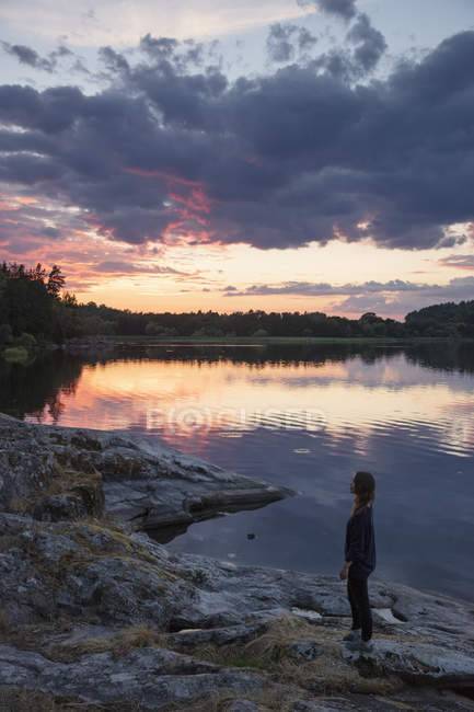 Femme debout au bord du lac Landsjon au coucher du soleil en Suède — Photo de stock