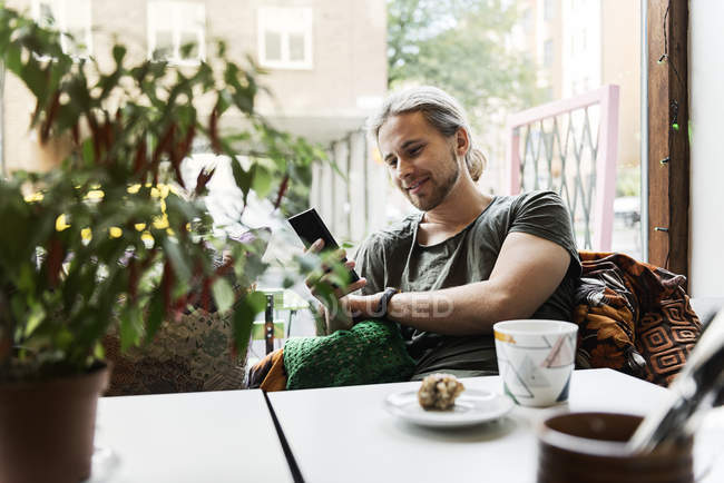 Hombre joven con teléfono inteligente en la cafetería, enfoque selectivo - foto de stock