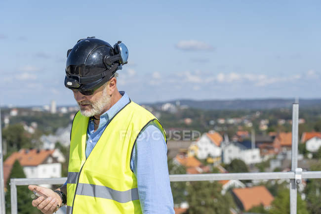 Trabajador de la construcción usando teléfono inteligente en el techo - foto de stock