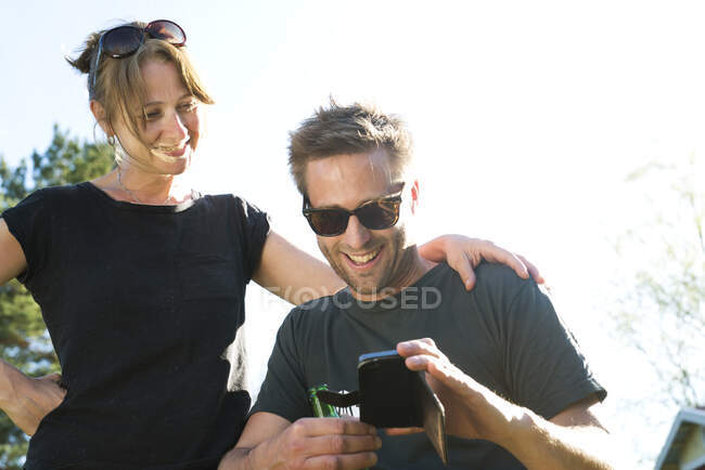 Parejas sonrientes y el uso de teléfonos inteligentes al aire libre - foto de stock