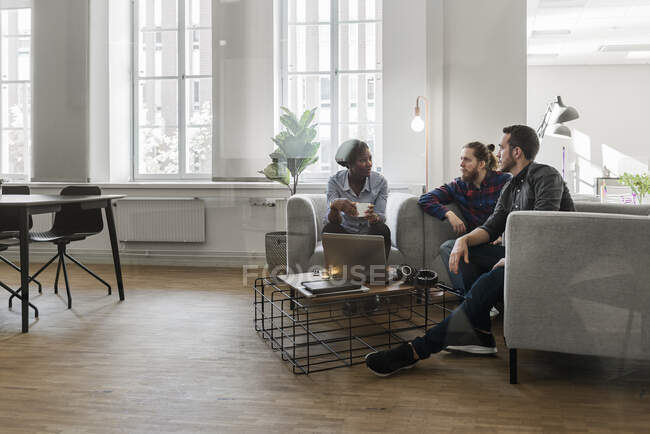 Compañeros de trabajo multiétnicos, hombres y mujeres que se sientan juntos y hablan en el cargo - foto de stock