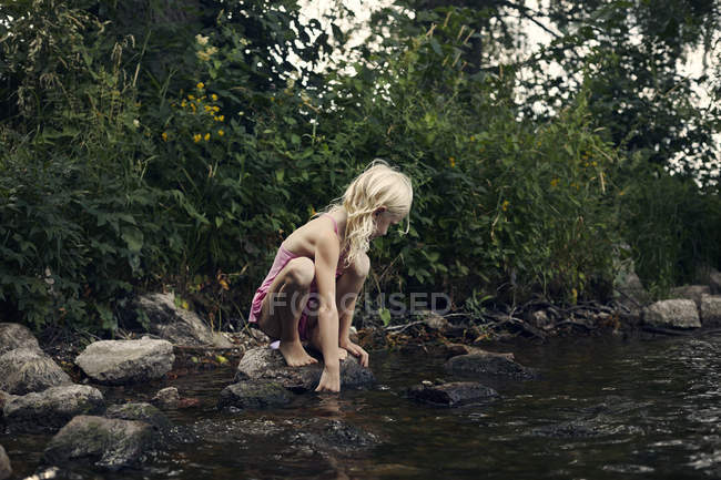 Vue latérale de fille accroupi par la rivière — Photo de stock