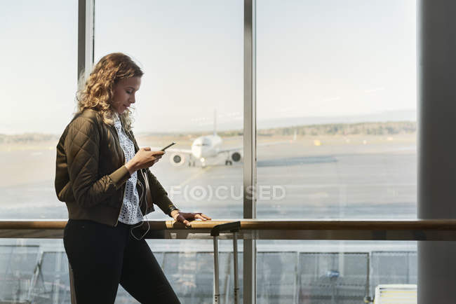 Жінка зі смартфоном біля вікна аеропорту — стокове фото