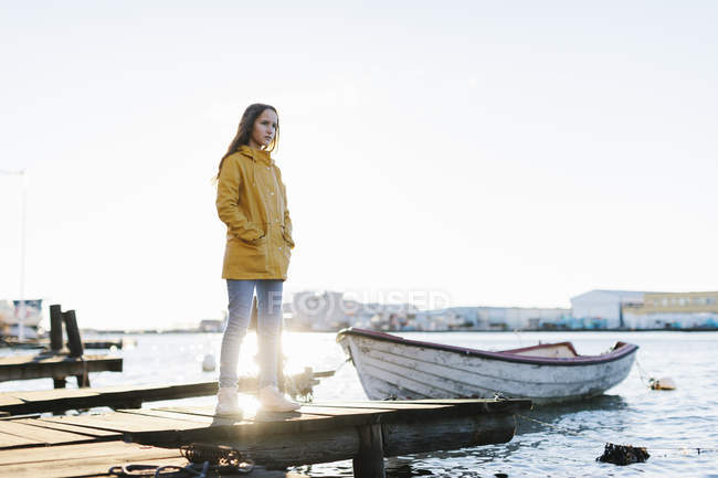 Chica vistiendo impermeable amarillo de pie en embarcadero - foto de stock