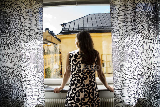 Femme regardant par la fenêtre, vue arrière — Photo de stock