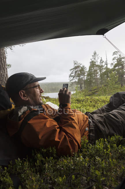Homme utilisant un téléphone intelligent dans une tente, foyer sélectif — Photo de stock