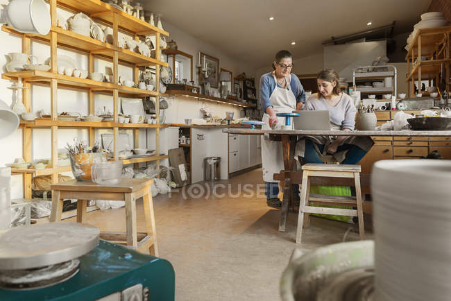 Las mujeres que utilizan el ordenador portátil en taller de cerámica - foto de stock