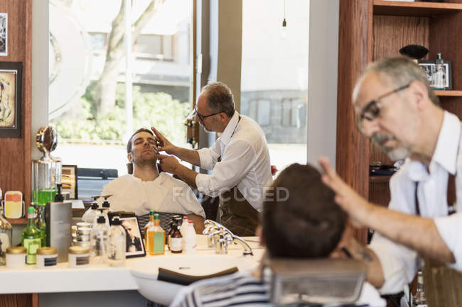 Парикмахер стрижет волосы молодого человека, избирательный фокус — стоковое фото
