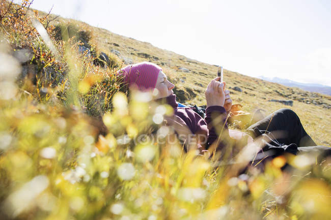Donna sdraiata in campo utilizzando smartphone — Foto stock