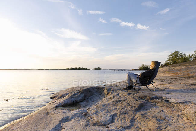 Mulher sentada na cadeira ao lado do mar — Fotografia de Stock