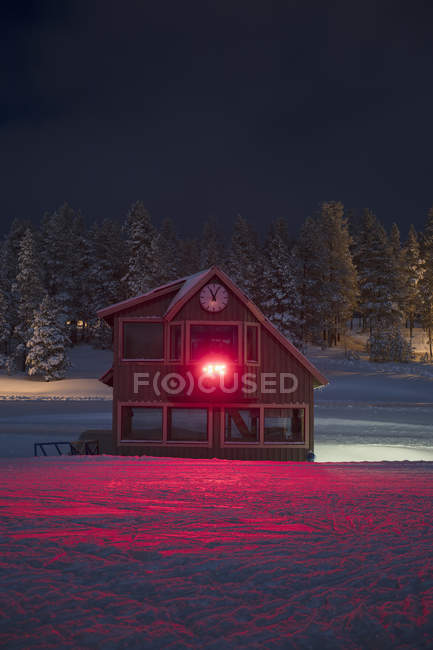 Cabaña de madera en nieve con luz roja - foto de stock